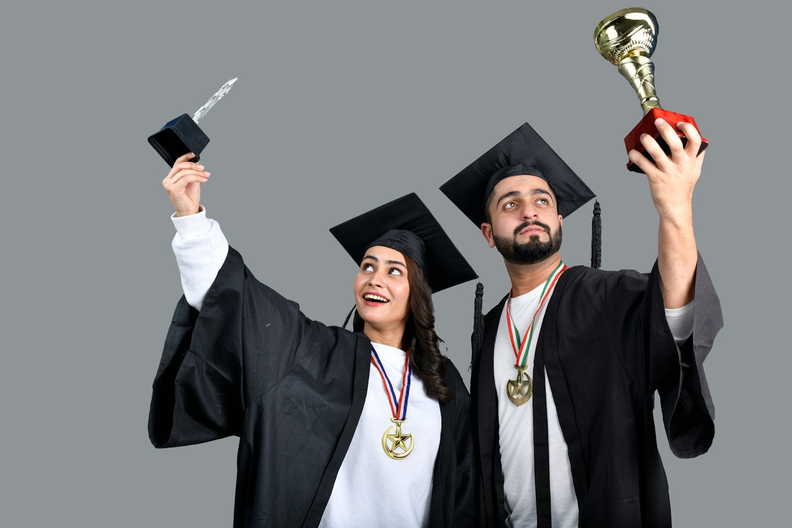 a man and woman wearing graduation gowns and holding a trophy